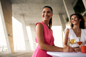 Two women drinking beverages, looking to the side and smiling.