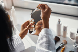 Person in a bathrobe applying a skincare serum with a dropper.